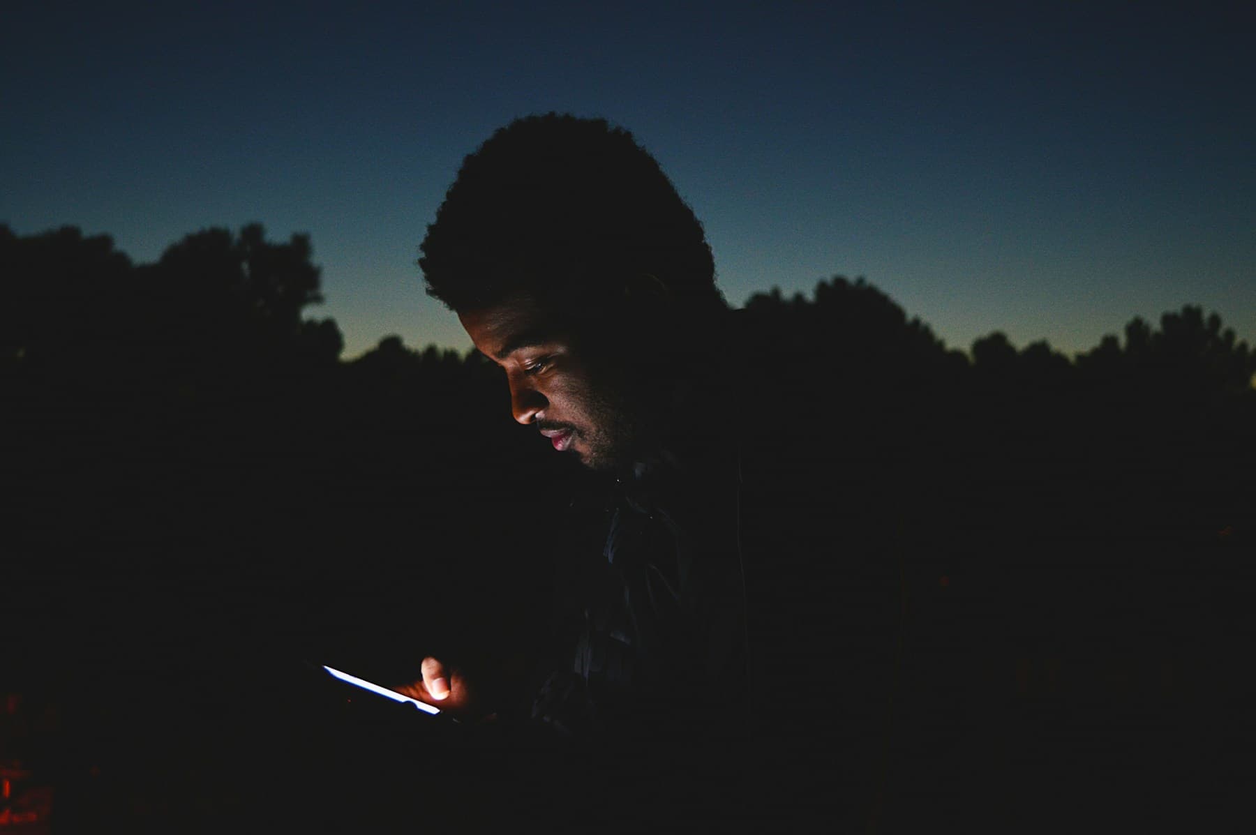 A man lit by his phone at dusk