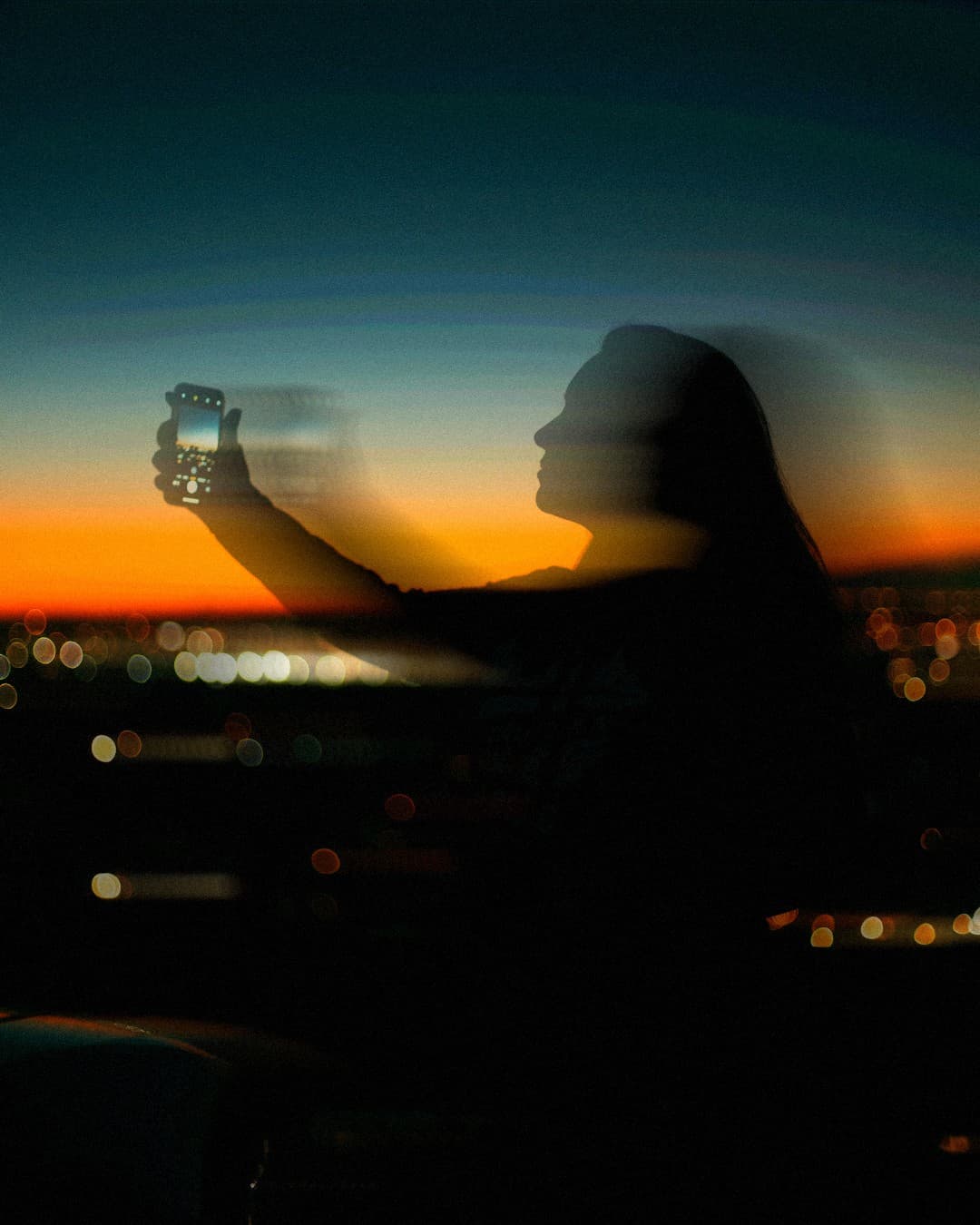 Silhouette holding up a phone against an orange sunset