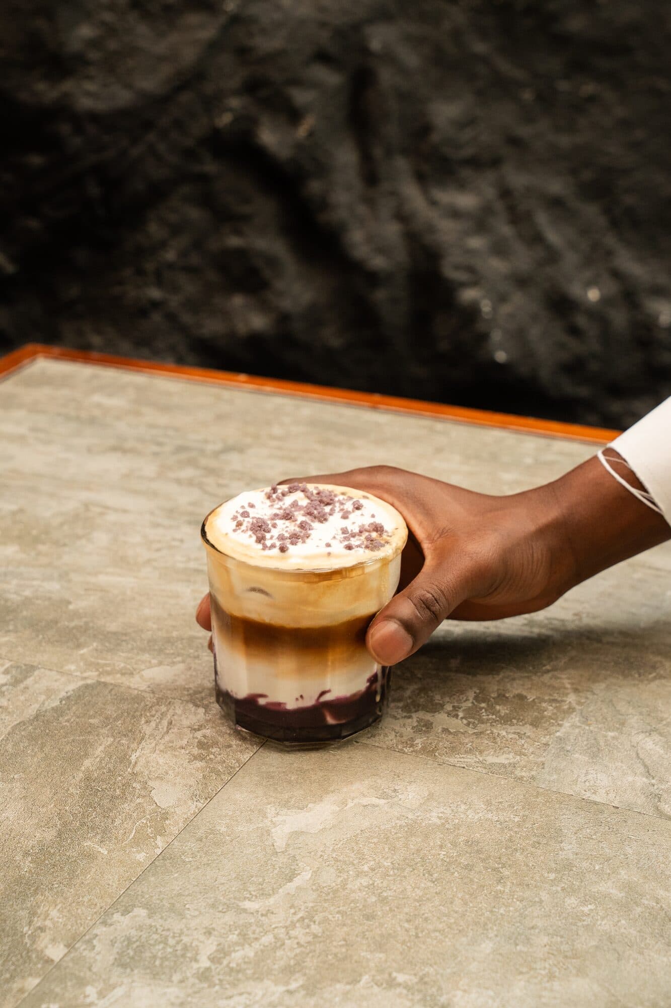 Hand holding an iced coffee on a marble table, Artisan Bakers